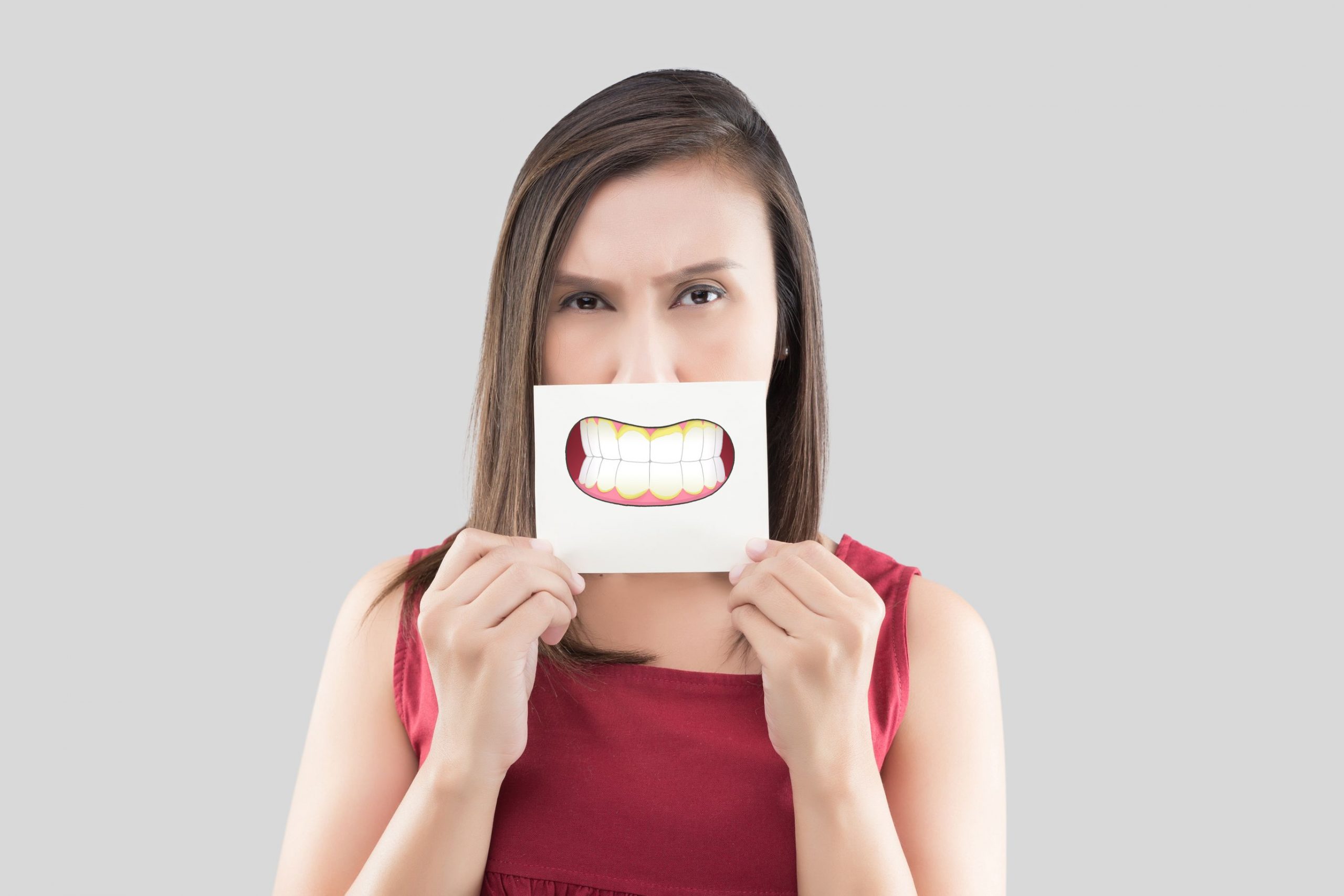 asian-woman-red-shirt-holding-brown-paper-with-dental-plaque-cartoon-picture-his-mouth-against-gray-wall-bad-breath-halitosis-concept-with-healthcare-gums-teeth (1)