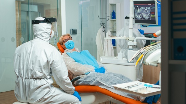 dentist-doctor-coverall-showing-senior-patient-x-ray-during-coronavirus-concept-new-normal-dentist-visit-coronavirus-outbreak-wearing-protective-suit-Let your dentist know your covid history